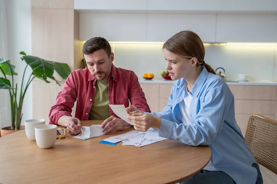 A couple reviewing bills at their kitchen table and wondering, “What is a billing address?